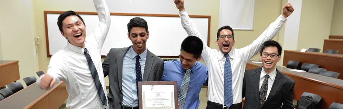 UCLA Law students holding a certificate and celebrating with their arms in the air