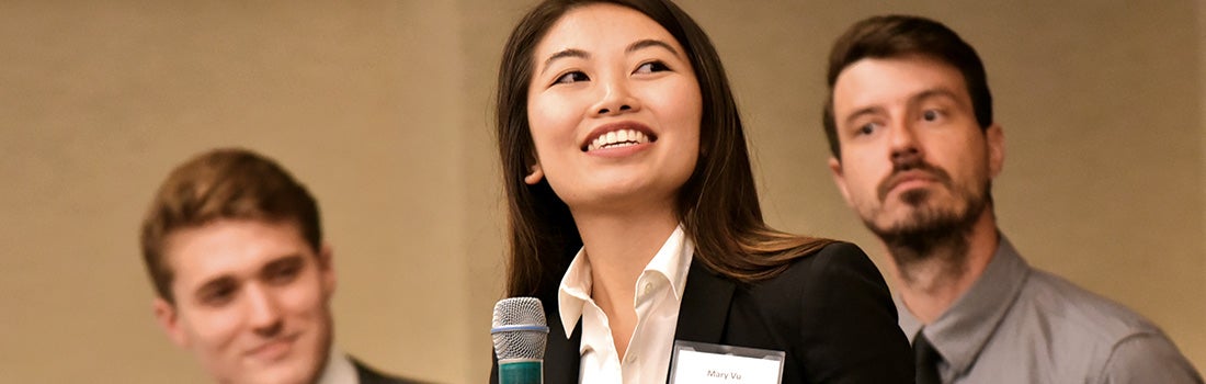 Student Mary Vu speaking into a microphone with two other student behind her