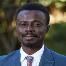 Headshot photo of Ayodele Babalola standing outside in front of green/leafy background