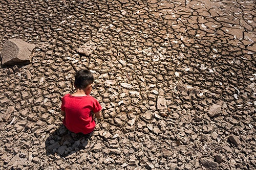 A child crouching on a parched piece of land